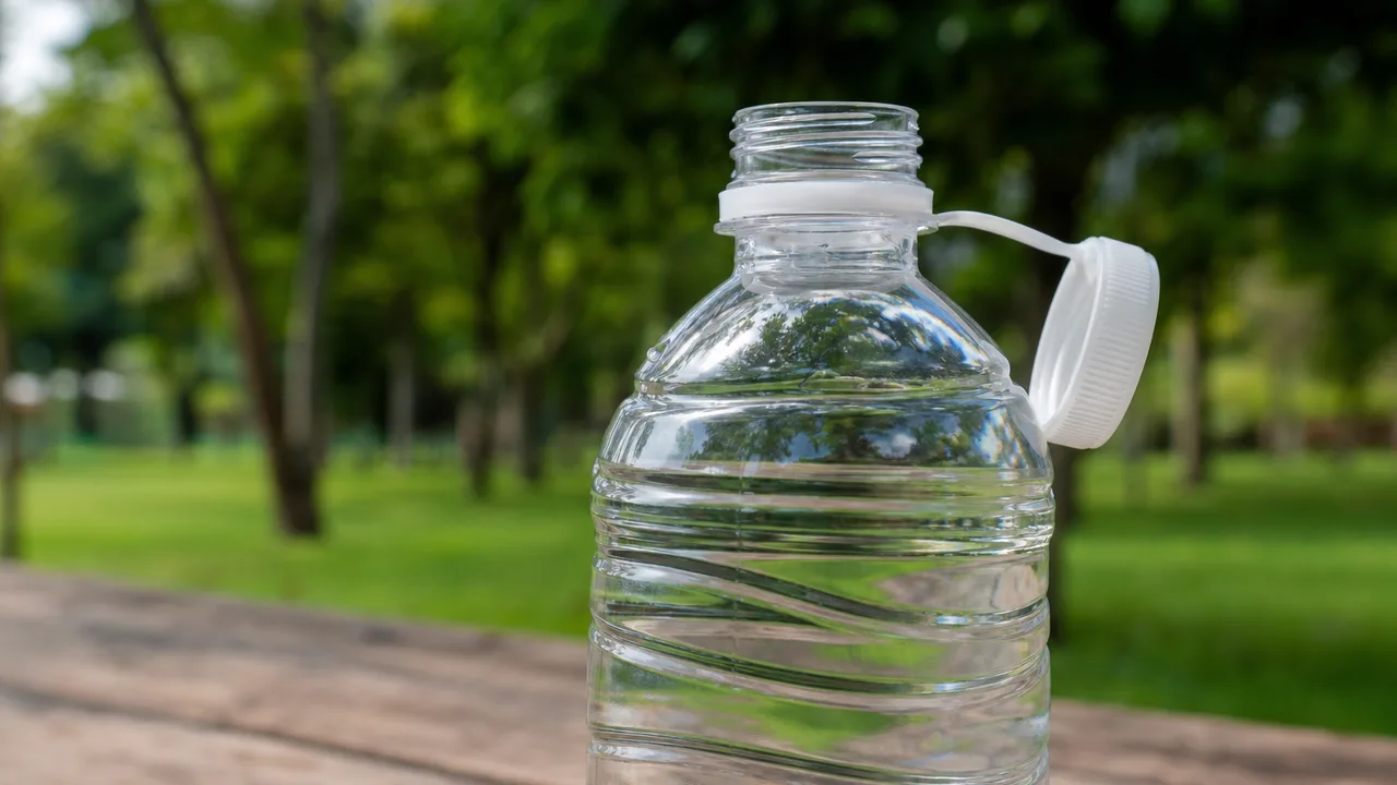 Gros plan sur une bouteille d'eau en plastique avec son bouchon attaché rabattu sur le côté, posée sur une table de pique-nique en extérieur, lumière naturelle