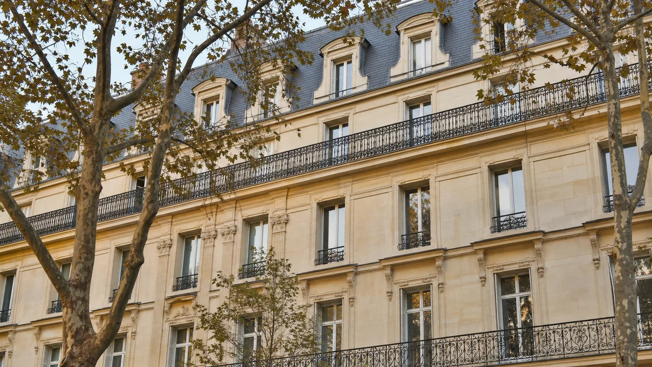 Façade d'immeuble haussmannien en pierre de taille avec balcons filants en fer forgé au deuxième et au cinquième étage, toit en zinc mansardé, lumière dorée de fin de journée